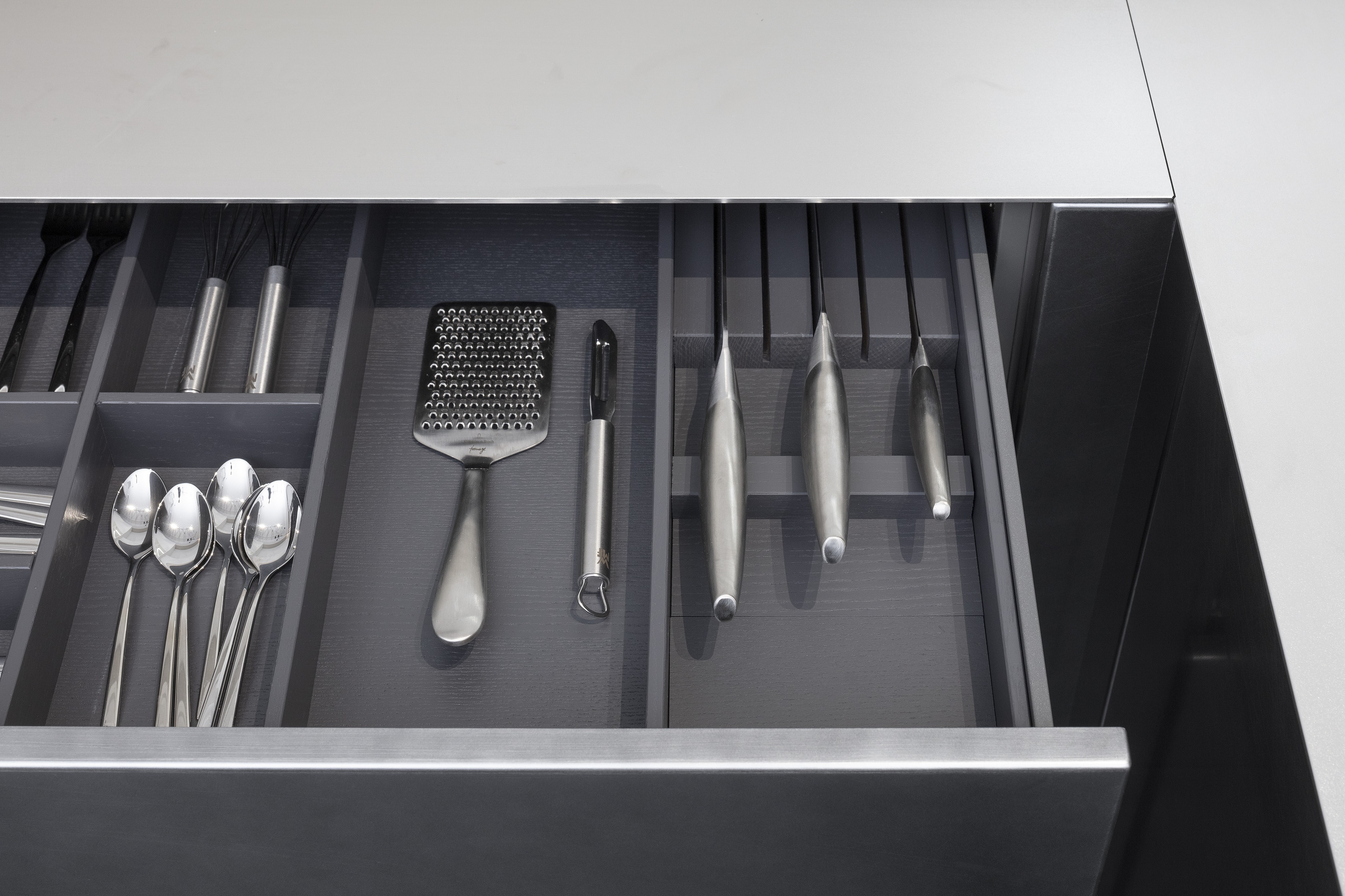 Front: Industriestahl Metalliclack geschliffen AV6000 NCS Mattlack APL: Franke Edelstahl 6 mm Geräte: Bora Spüle Armaturen: Franke  Features: Metallfront, Spülbecken in APL integriert (aus einem Guss), Oberschränke mit Lowboard-Charakter, integrierter Arbeitsplatz, dunkler Korpus mit Aluminium-Abschlussleiste, Wärmeschublade mit Gittereinsatz.