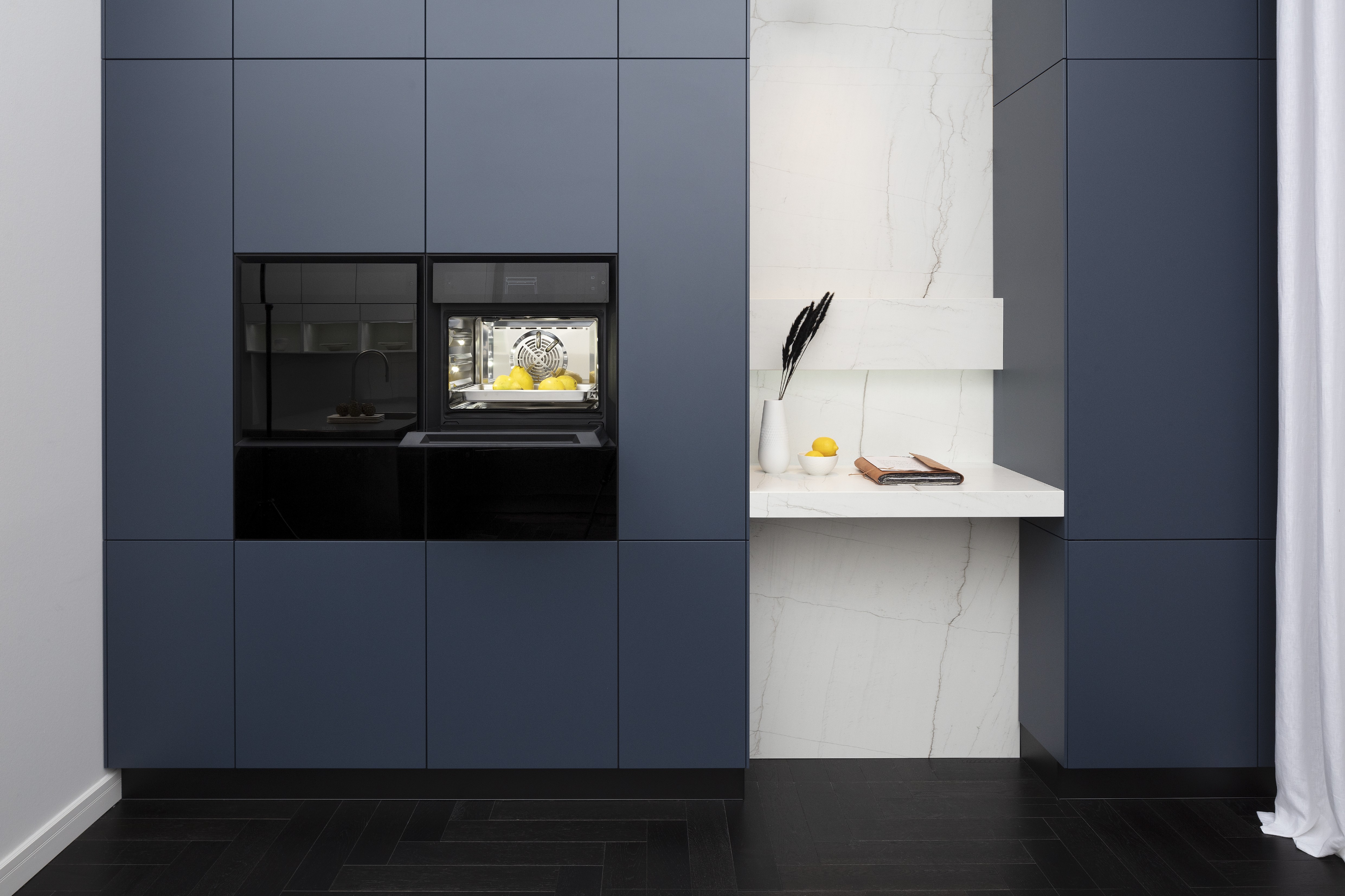 Front: Industriestahl Metalliclack geschliffen AV6000 NCS Mattlack APL: Franke Edelstahl 6 mm Geräte: Bora Spüle Armaturen: Franke  Features: Metallfront, Spülbecken in APL integriert (aus einem Guss), Oberschränke mit Lowboard-Charakter, integrierter Arbeitsplatz, dunkler Korpus mit Aluminium-Abschlussleiste, Wärmeschublade mit Gittereinsatz.