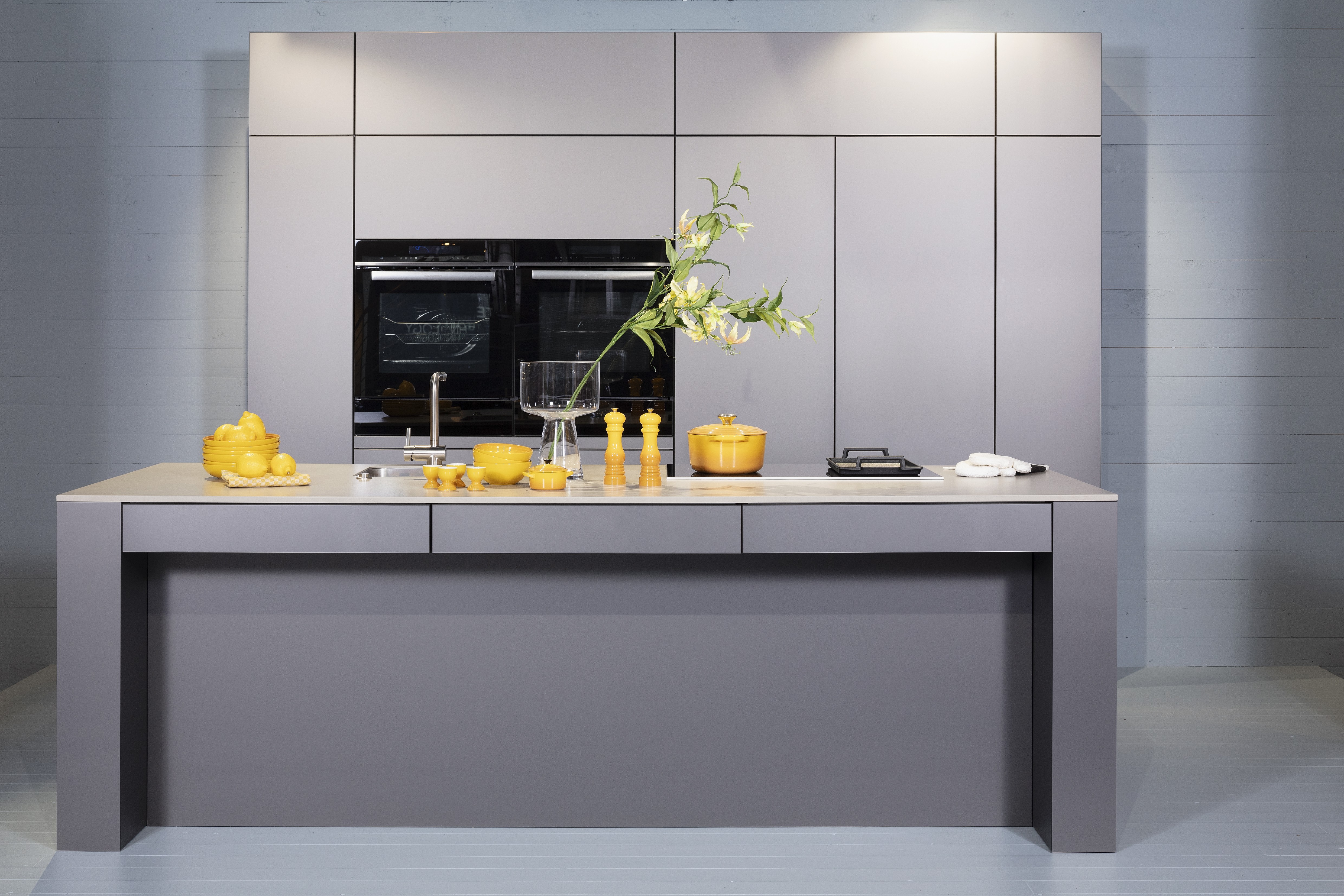 Concept130ART Front: SMART-GL Sandgrau metallic APL: SMART-GL Carbon metallic Geräte Blaupunkt Armatur und Spüle: Franke  Features: Insellösung mit Thekenfunktion mit Schubladen, Teppanyakiaufsatz für Kochfeld, Schubladen in Silber, Schubladen mit Griffmulde, Nischenlösung in Blau mit Regalfunktion.