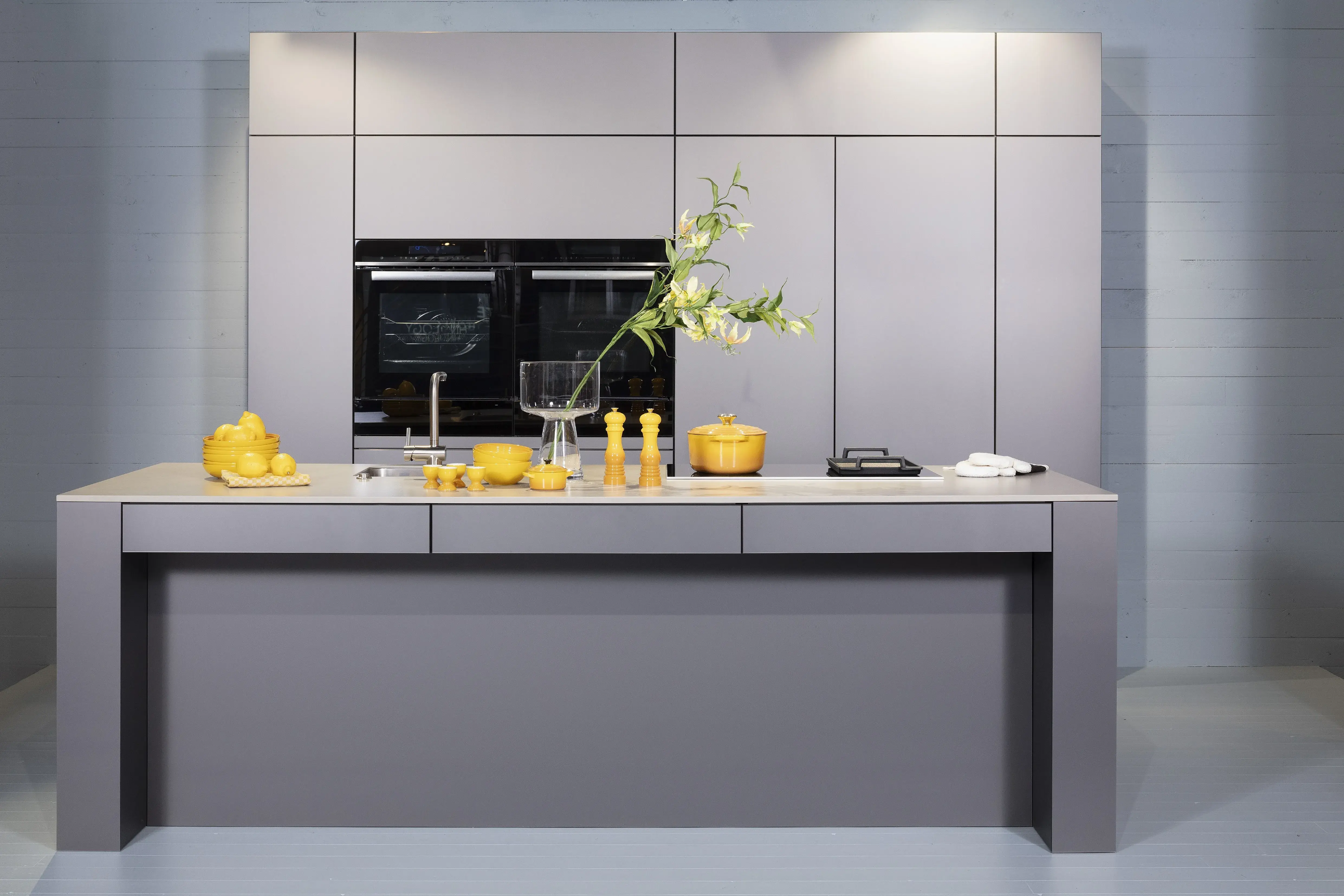 Concept130ART Front: SMART-GL Sandgrau metallic APL: SMART-GL Carbon metallic Geräte Blaupunkt Armatur und Spüle: Franke  Features: Insellösung mit Thekenfunktion mit Schubladen, Teppanyakiaufsatz für Kochfeld, Schubladen in Silber, Schubladen mit Griffmulde, Nischenlösung in Blau mit Regalfunktion.